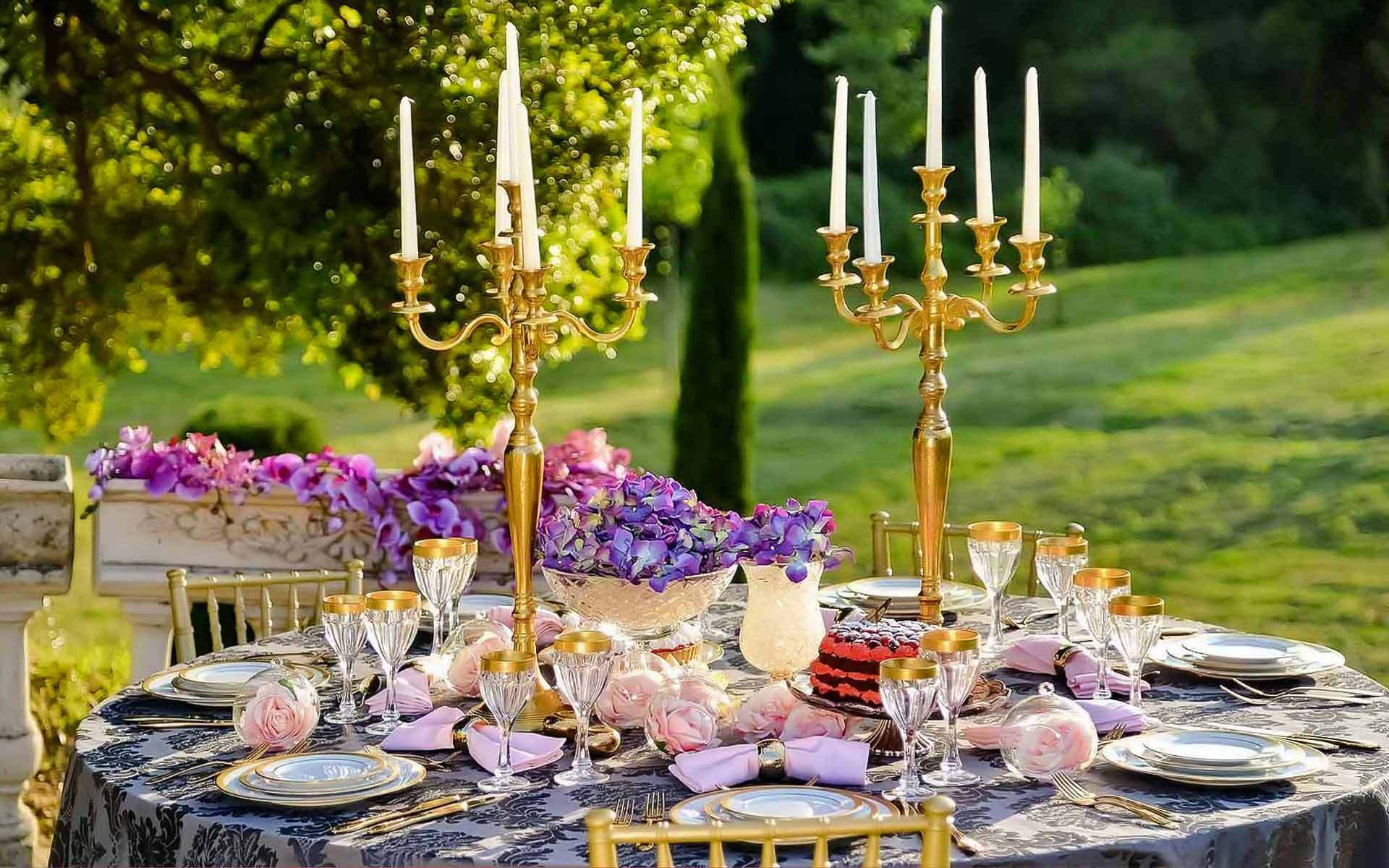 Beautiful reception table setting – Gold candelabras with ivory candles and white and purple floral arrangement by Rogdaki Events Trademark