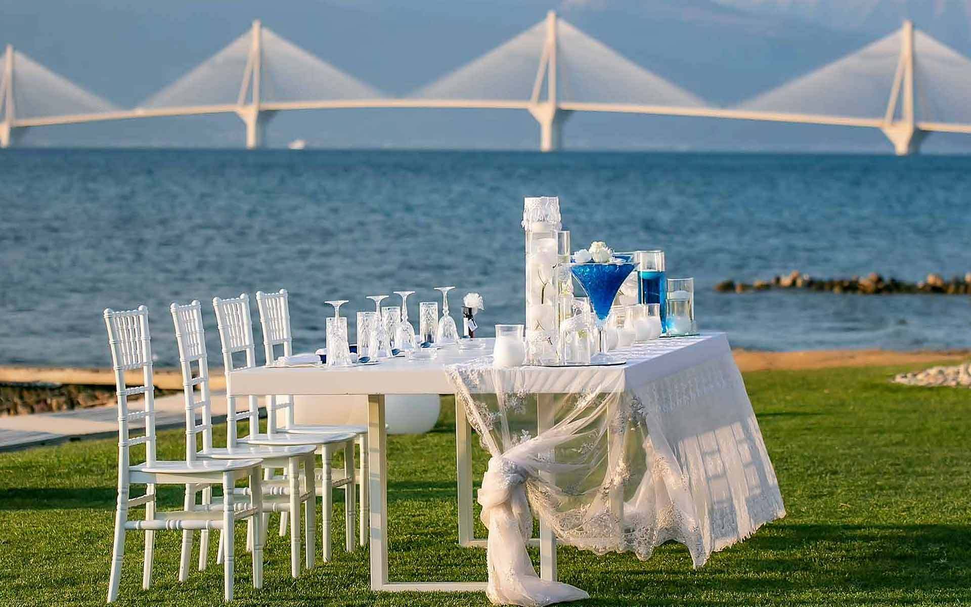 Unique, beach, simple table centerpiece with the biggest bridge in Greece as a background by Rogdaki Events Trademark