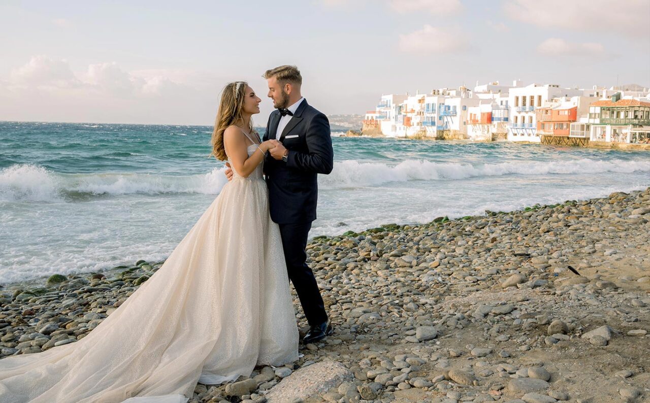 Γαμήλιος προορισμός Μύκονος 5 Ρομαντικό ζευγαρο πορτρέτο στη Μικρή Βενετία, με το κύμα και την πόλη της Μυκόνου ως φυσικό σκηνικό.
