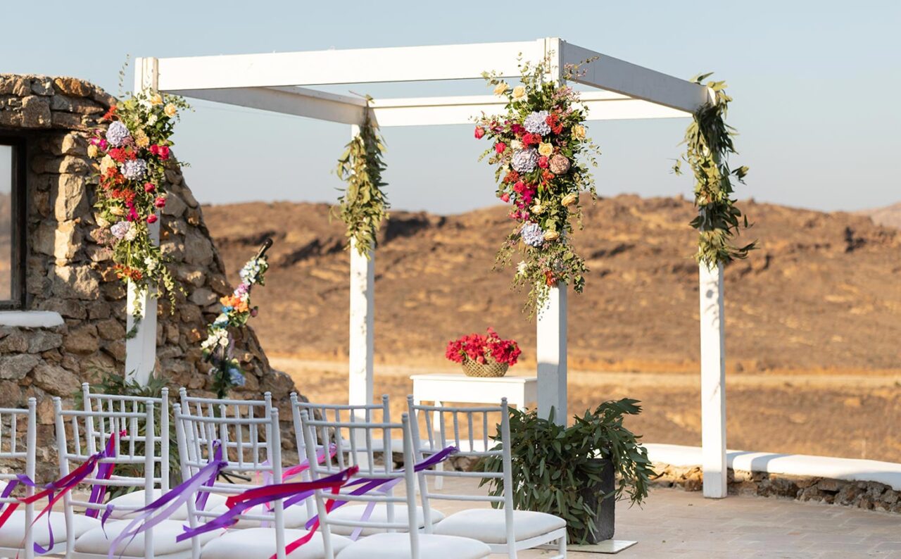 Γαμήλιος προορισμός Μύκονος 6 Στολισμός Μυστηρίου με χρωματιστά λουλούδια, ιδανικό για ζευγάρια που θέλουν ζωντανή, χαρούμενη ατμόσφαιρα.