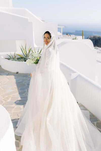 Elegant bride walking through the whitewashed paths of Santorini before her destination wedding ceremony.