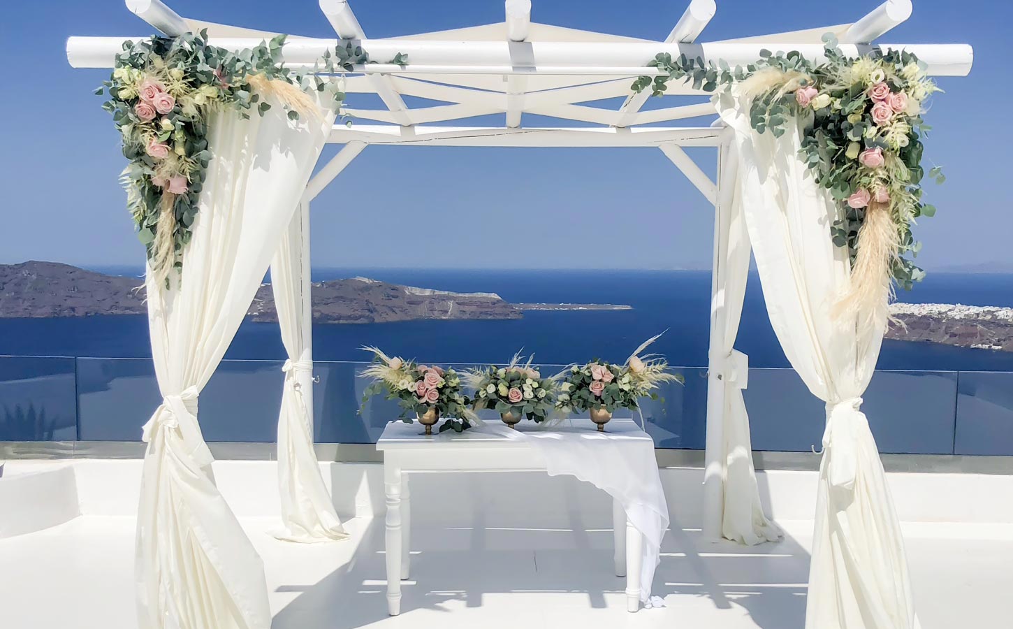Κομψό σκηνικό γαμήλιας τελετής σε gazebo με θέα την καλντέρα, σχεδιασμένο για ένα stylish destination wedding στη Σαντορίνη