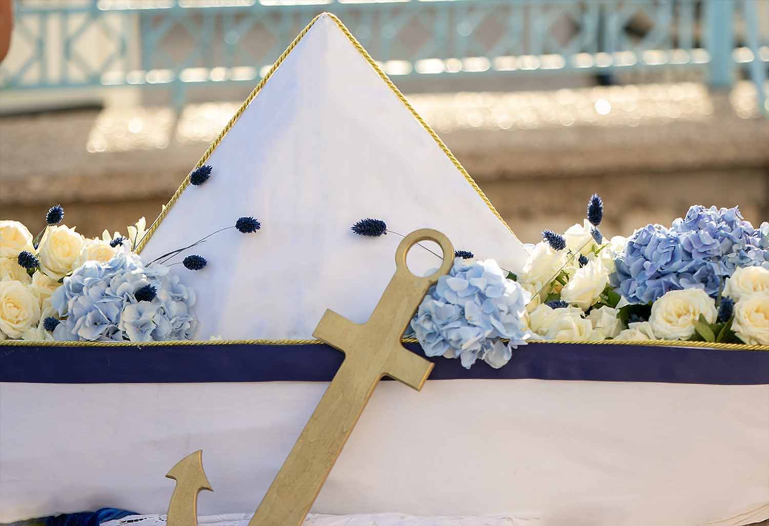 A handmade boat made out of white fabrics decorated with natural white and blue flowers and a wooden gold anchor