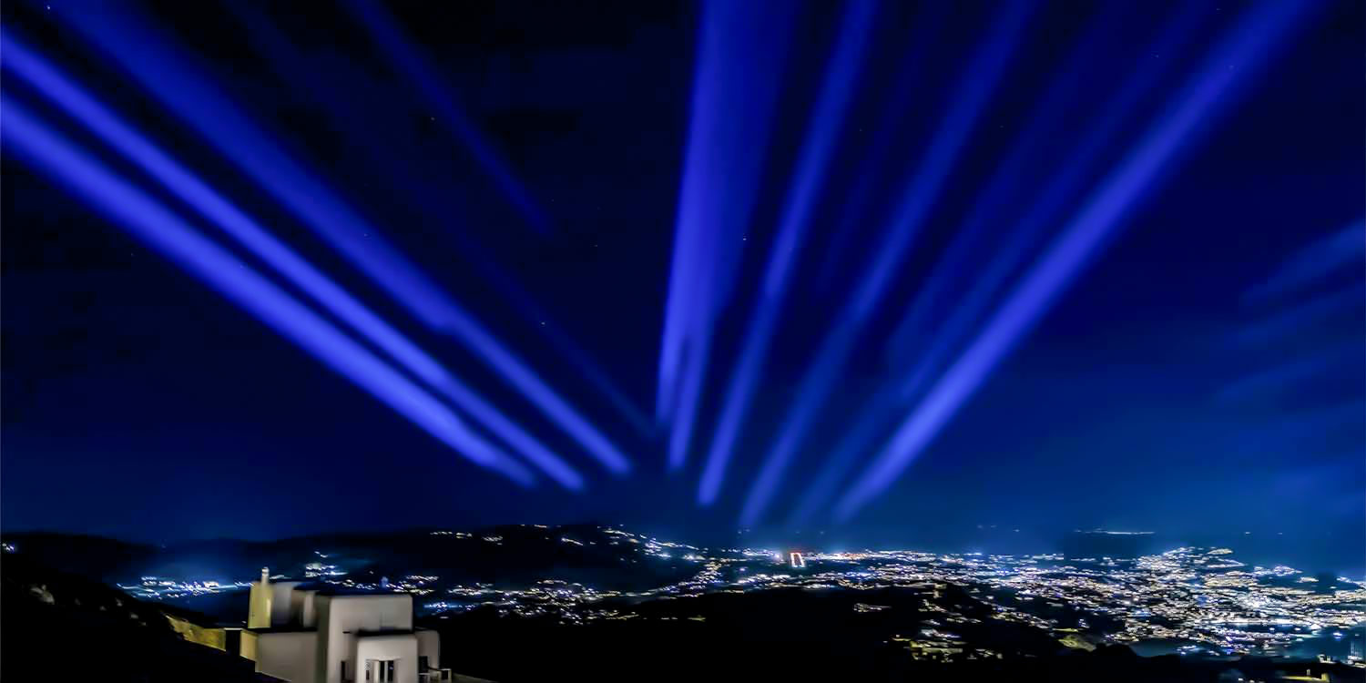 A breathtaking nighttime view of the Mykonos landscape with brilliant blue beams of light illuminating the sky by Rogdaki Events for a Mykonos private villa wedding