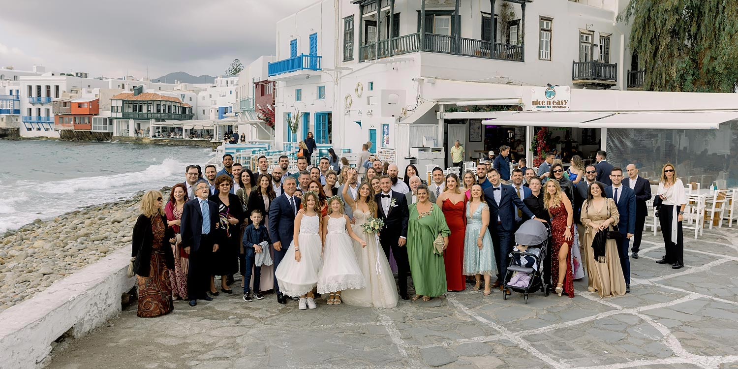 Πολυτελής Γάμος στη Μύκονο 14 A joyful group photo by the sea embracing love. Mediterranean Romance in Mykonos by Rogdaki Events