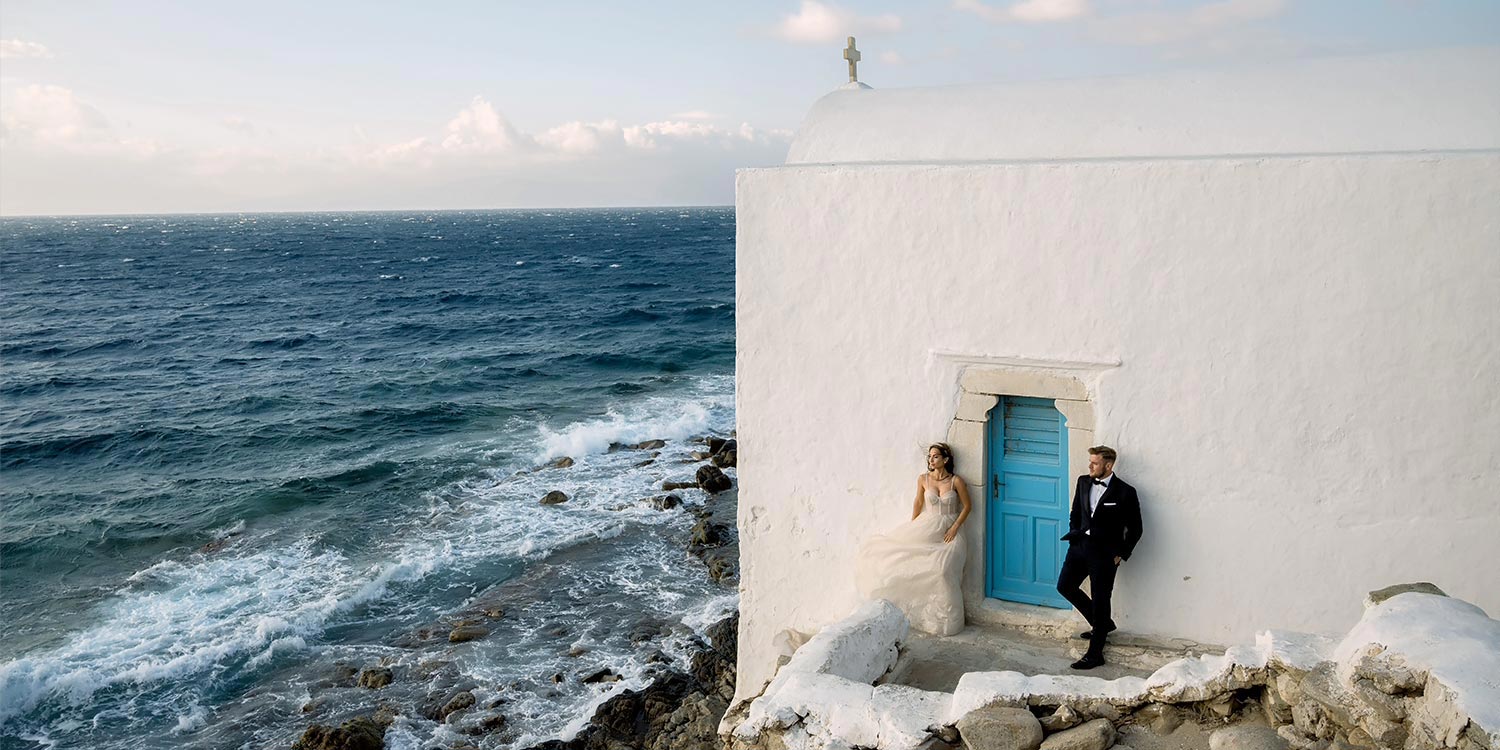 Πολυτελής Γάμος στη Μύκονο 17 Bride and groom by the chapel kissed by waves. Mediterranean Romance in Mykonos by Rogdaki Events