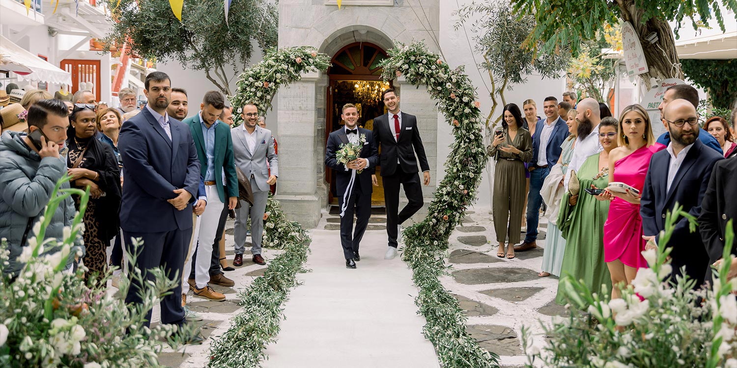 Πολυτελής Γάμος στη Μύκονο 10 Groom walks proudly under a floral archway. Mediterranean Romance in Mykonos Rogdaki Events