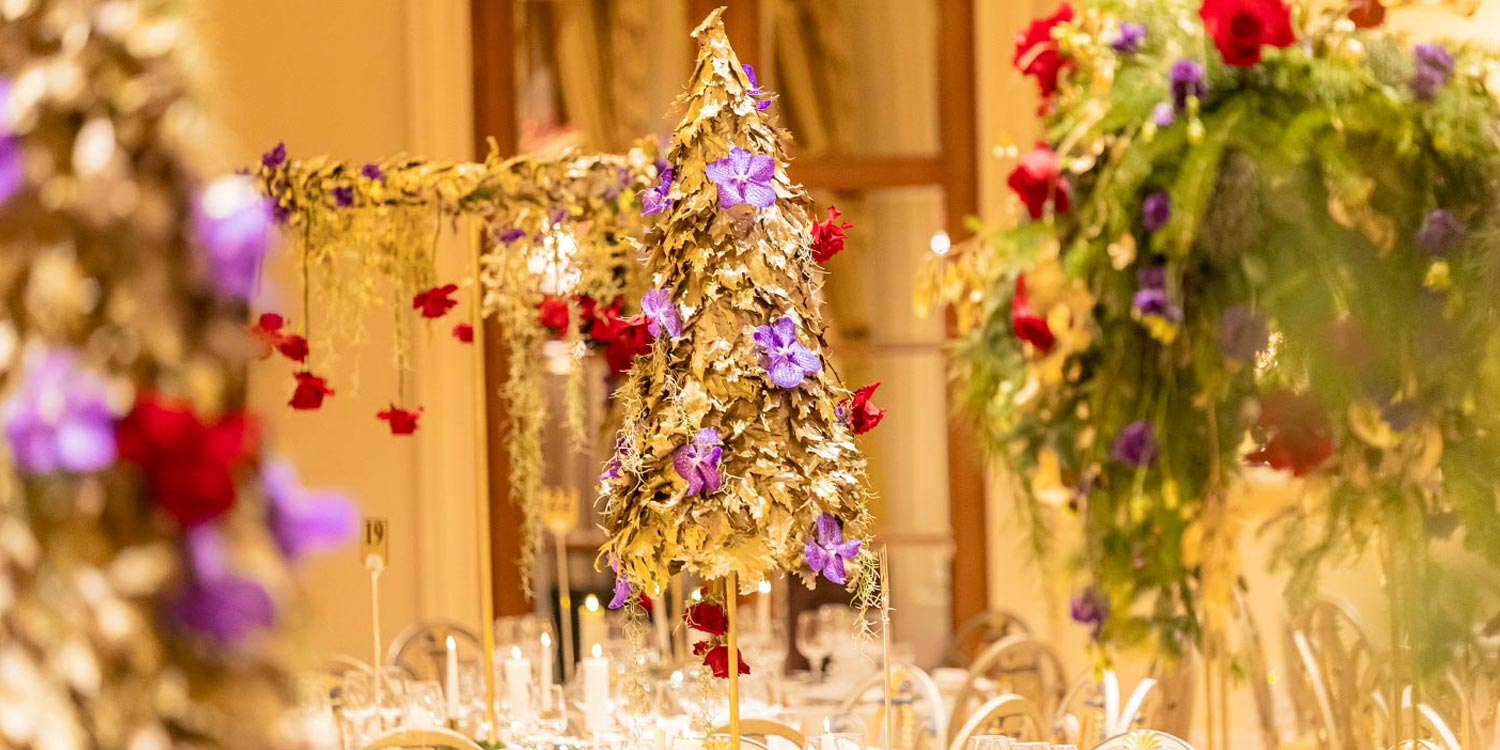 Hotel Grande Bretagne – 150 Χρόνια Ιστορίας 17 Golden tree centerpieces embellished with red roses and purple orchids by Rogdaki Events bring festive grandeur to the ballroom of the Grande Bretagne