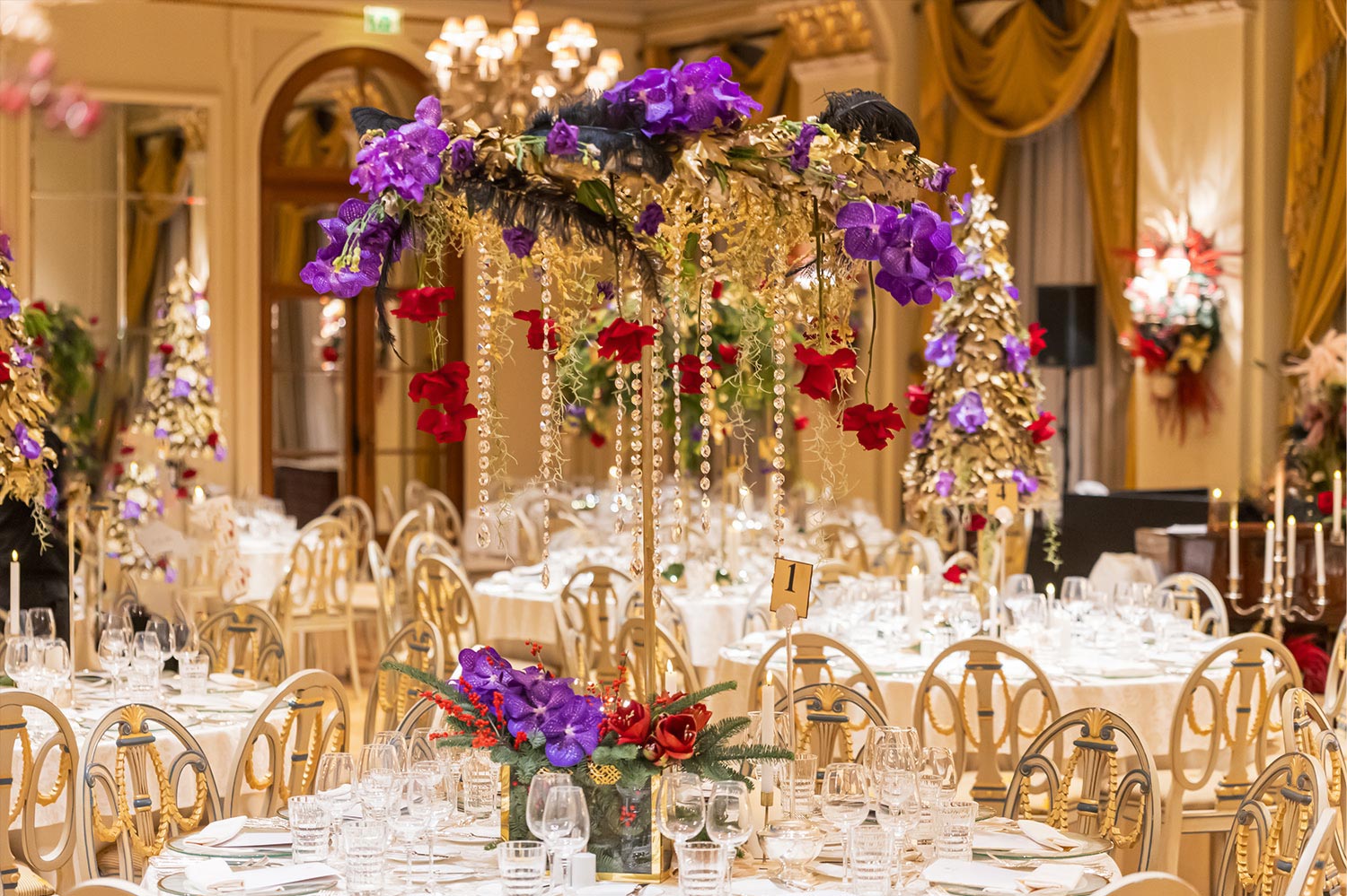 Hotel Grande Bretagne – 150 Χρόνια Ιστορίας 18 Lavish gold, red, and purple floral arrangements by Rogdaki Events cascade with crystals, transforming the Grande Bretagne ballroom into a luxurious gala dinner scene