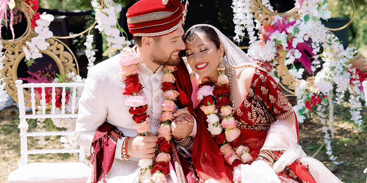 Indian Wedding in a Private Villa, by Rogdaki Events — laughter and love shine through as the newlyweds sit adorned with garlands, surrounded by lush floral decor