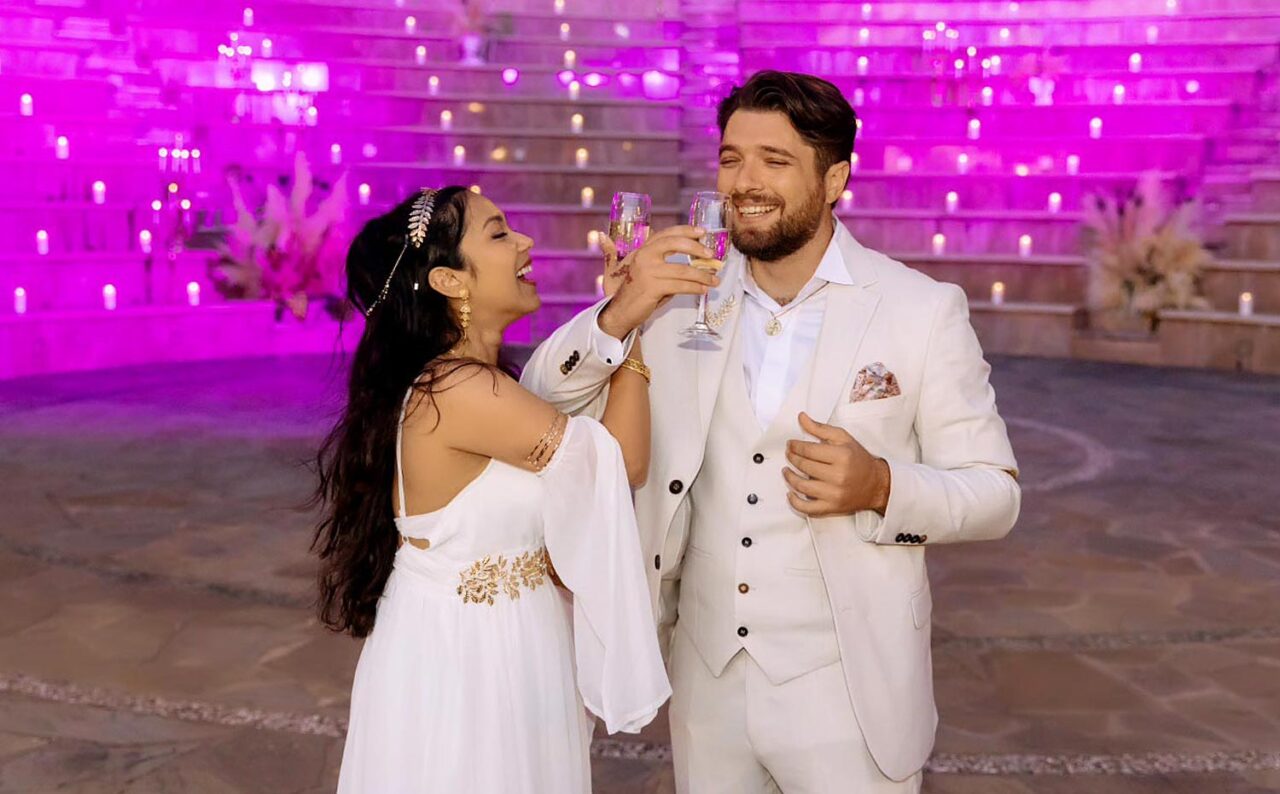 Joyful toasts under violet skies during the Ancient Greek Wedding in an Amphitheater by Rogdaki Events, as the couple celebrates amidst a romantic candlelit setting
