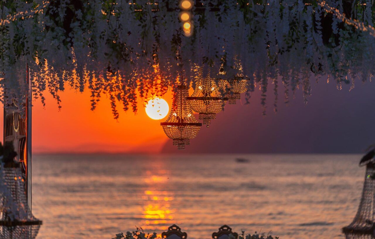 Crystal chandeliers framing a glowing sunset at a Luxury Seaside Wedding in Greece by Rogdaki Events