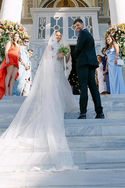 Rogdaki Events, chic & colorful γάμος, το ζευγάρι στα σκαλιά της εκκλησίας με εντυπωσιακό μακρύ πέπλο η νύφη.