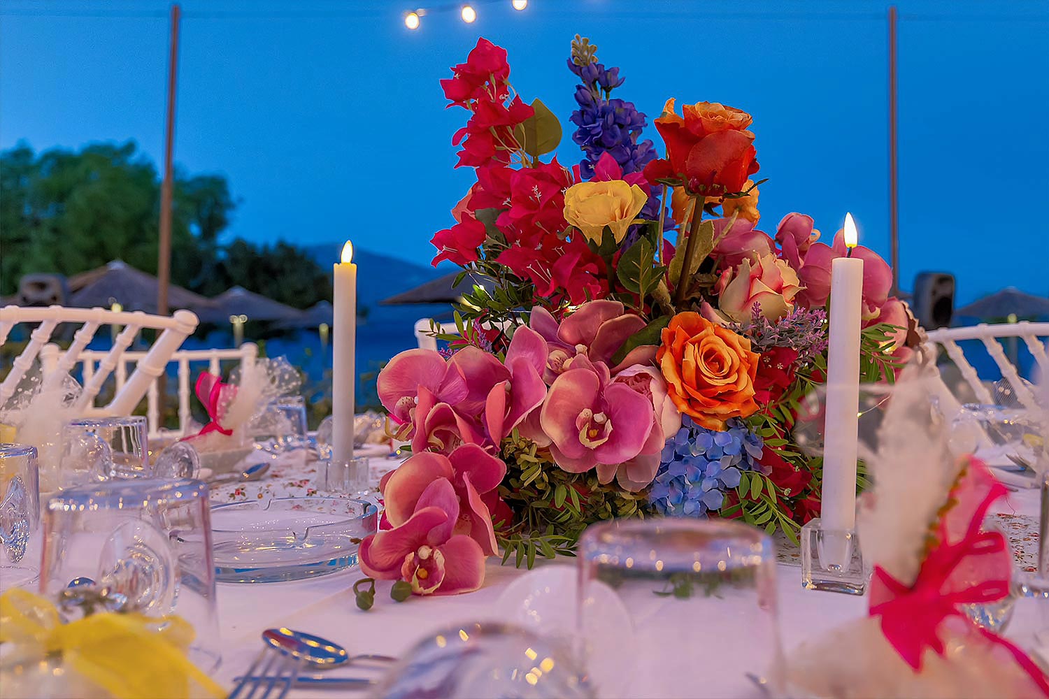 Chic & Colorful Γάμος στο Κτήμα Παναγιωτόπουλου 47 Rogdaki Events, μια ανθοσύνθεση με ορχιδέες και τριαντάφυλλα, που αντανακλά την πολύχρωμη και ρομαντική ατμόσφαιρα του δειλινού.