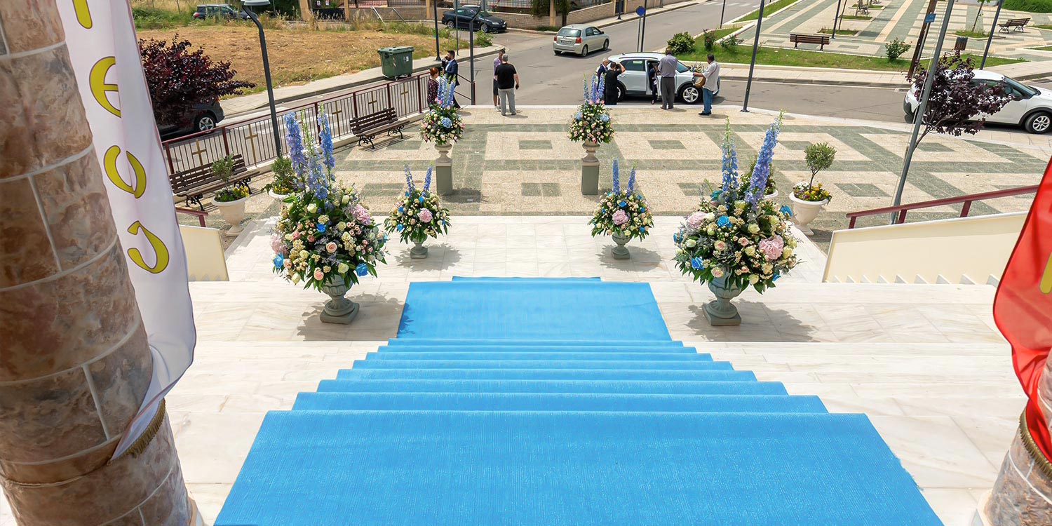 A Signature Wedding & Baptism Production in Blue 5 A dreamlike entrance at Agia Varvara in Agrinio, featuring a blue carpet and lush floral arrangements by Rogdaki Events.