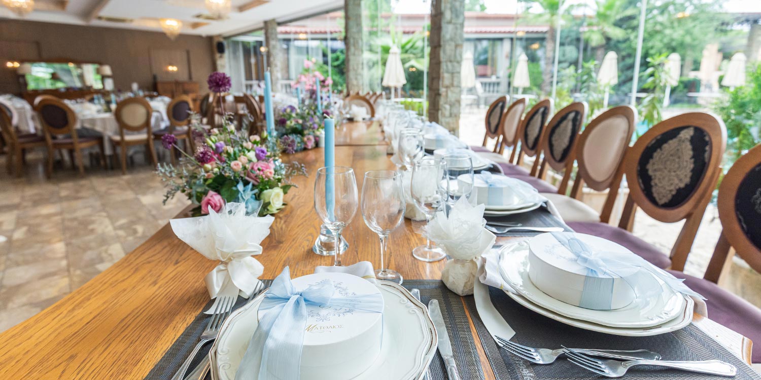 A Signature Wedding & Baptism Production in Blue 25 Wedding at Korali, Agrinio, signed by Rogdaki Events, featuring a wooden tables, blue candles, floral arrangements, and baptism favors.