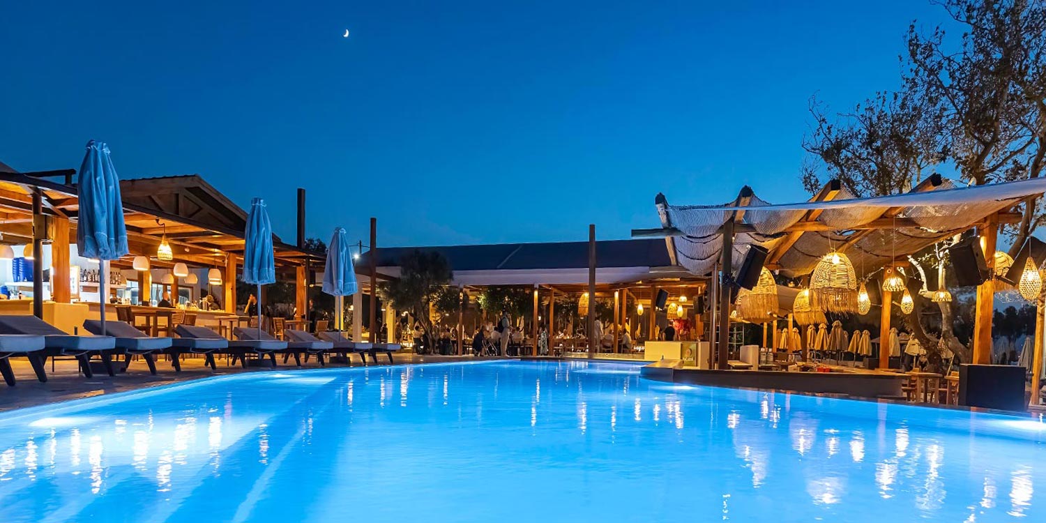 Nighttime ONA poolscape curated by Rogdaki Events, glowing with warm light and serene coastal atmosphere.